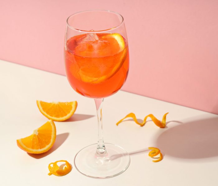 Concept of summer cocktail, Aperol Spritz on white table against pink background